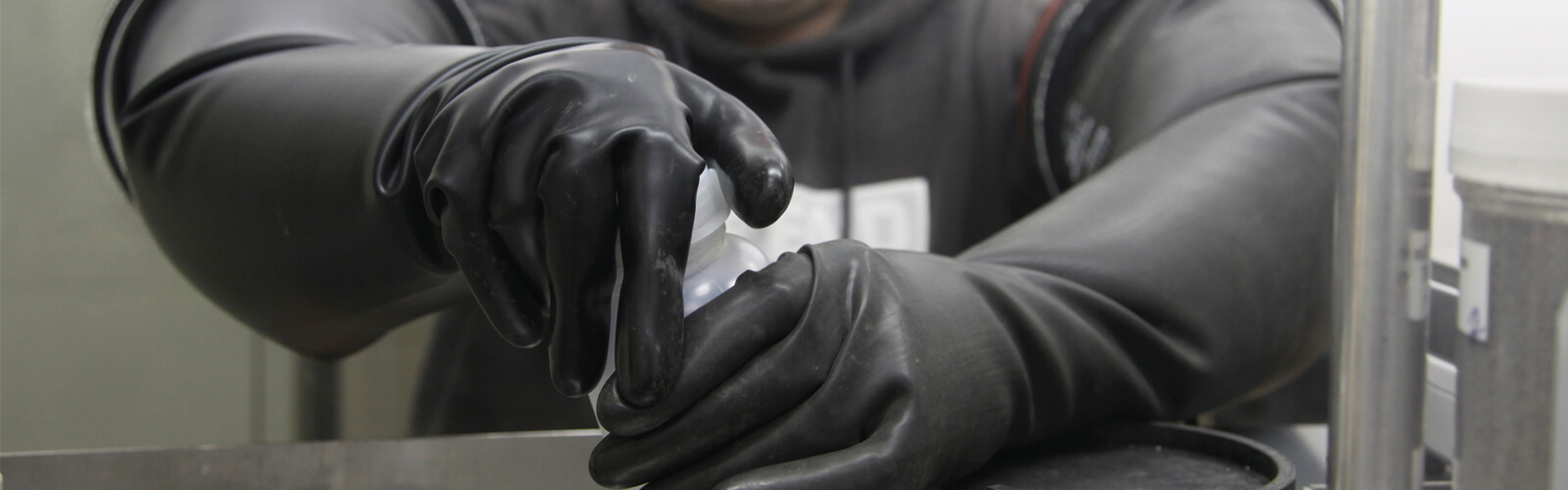 Mitarbeiter mit Glovebox Pharma Handschuhen schraubt einen Behälter zu
